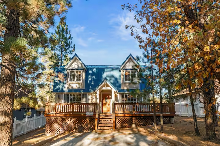 The HappyNest cabin in autumn, golden oaks and pines around the blue A-frame and its wraparound deck